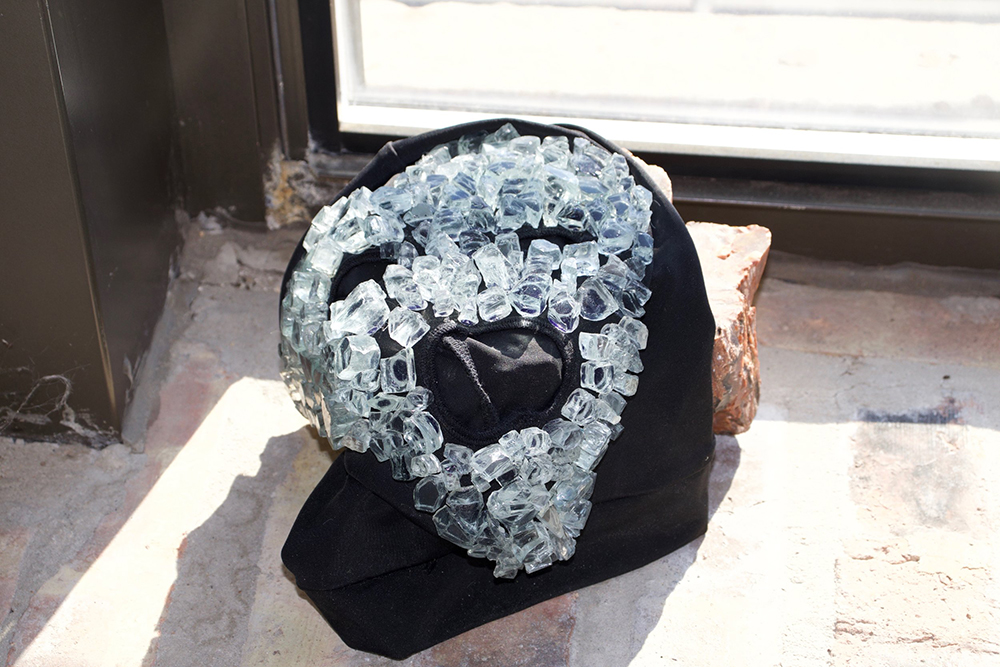A black ski mask with glass shard glued to it resting on a brick in the sun